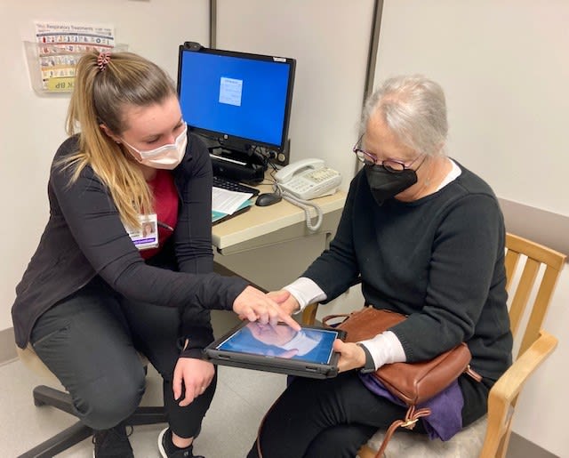 Caitlin Gard helping a patient holding a tablet while sitting side-by-side in a medical clinic.