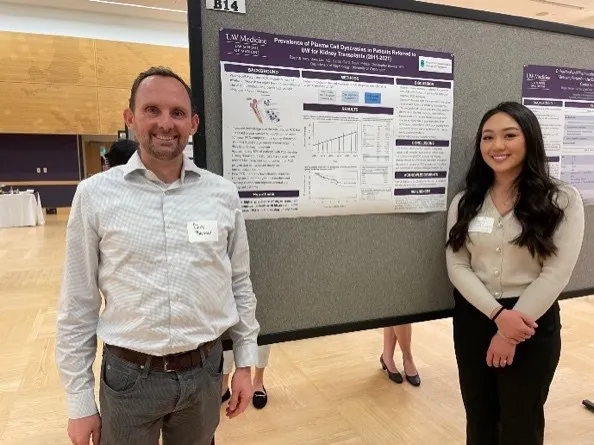 Dr. Blosser and Regina Tsay smiling, standing on either side of a research poster in a conference hall.